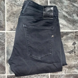Replay Anbass jeans - Svarta Replay Anbass jeans i slim fit med klassisk femficksdesign och diskret R-logga på bakfickan. Jeansen har smal passform, raka ben och är tillverkade i stretchigt bomullsmaterial för extra komfort. Midja 40cm, längd 110cm. JAG SKICKAR EJ FLER BILDER NÄR JAG BÄR JEANSEN! för storleksguide hänvisar jag till måtten och för bättre inblick i passformen rekommenderar jag att googla på modellnamnet. Jeansen kan vara uppsydda utan att jag noterat det så kolla måtten noggrant :) S4