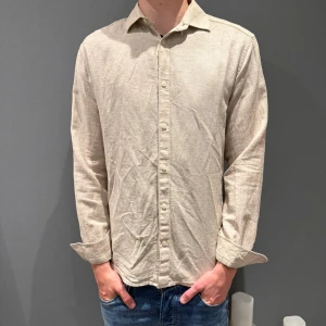 Beige linneskjorta med knappar - Snygg beige skjorta i linne med klassisk krage och knappar hela vägen framtill. Skjortan har lång ärm och en avslappnad passform som funkar perfekt till jeans. Enkel och stilren design som är lätt att matcha.