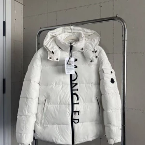Vit pufferjacka från Moncler - Säljer en vit pufferjacka från Moncler med stor logotyp längs dragkedjan. Jackan har huva med snörning, långa ärmar och två sidofickor med dragkedja. Perfekt för kalla dagar och har en modern, clean look.