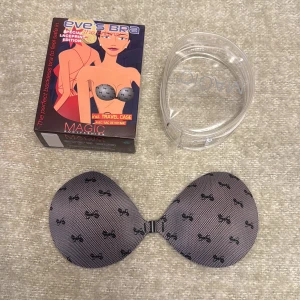 Svart bandlös bh stl.B från Magic Bodyfashion - Säljer en svart  bandlös bh B från Magic Bodyfashion, modell Eve's bra. Smarta, självhäftande kupor som gör bysten något större och ger en bra push up-effekt. Kuporna är följsamma och fäster bra på kroppen. Smart t ex under en rygglös klänning eller topp.Kommer med en praktisk reseförpackning. 