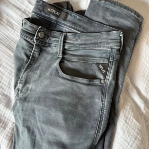 Replay grå jeans slim fit 31/32 - Snygga grå jeans från Replay i modellen M914 slim fit. Jeansen har klassisk femficksdesign, dragkedja och knappstängning. Materialet är mjukt och stretchigt jeans, vilket gör dem riktigt sköna att bära. Passar dig som gillar en smalare siluett.