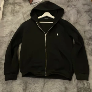 Svart hoodie från Polo Ralph Lauren - Svart hoodie från Polo Ralph Lauren med dragkedja och huva. Använt fåtal gånger så den är typ som ny. Pris kan diskuteras vid snabb affär och tveka inte på att kontakta vid frågor!