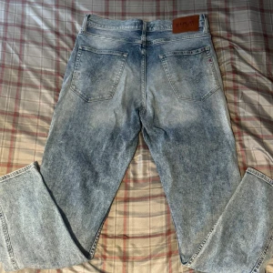 Replay ljusblå jeans straight fit - Säljer ett par ljusblå Replay jeans med snygg tvättad look och klassiska fem fickor. Modellen har rak passform och normal midja, med Replay-logga på läderpatch baktill. Perfekta för dig som gillar stilrena och bekväma jeans.