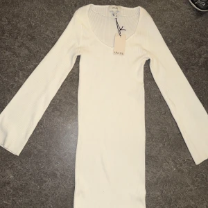 Vit ribbad långärmad klänning AWARE - Supersnygg helt ny vit ribbad klänning från AWARE med lång och bred ärm och v-ringad hals. Modellen är figurnära och har en stilren, enkel design som är lätt att matcha med accessoarer. Den är även lite tjockare i materialet. Perfekt för dig som gillar minimalistisk stil och vill ha en klänning som sticker ut med sin rena look.