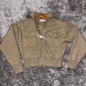 Beige stickad kofta från Bershka - Snygg beige stickad kofta från Bershka med dragkedja framtill och två stora fickor på bröstet. Modellen är croppad med ribbade muddar och krage som ger en chill vibe. Perfekt att slänga på sig när det är lite kyligt ute.priset går att diskuteras 💕