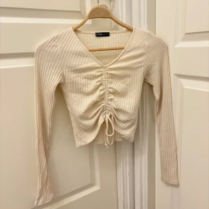 Beige ribbad omlottopp med snörning - Säljer en beige ribbad topp med lång ärm och snygg v-ringning. Toppen har omlottdetalj och snörning framtill. Skriv för fler bilder💕