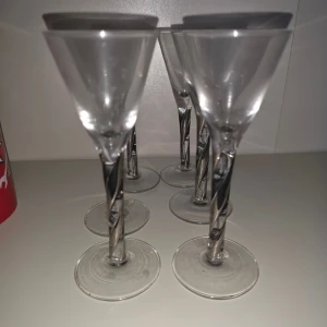 Snapsglas - Bilden visar ett set med sex eleganta snapsglas med spiralformad fot. Glasen är genomskinliga och har en unik design på stjälken. Perfekta för fest eller middagsbjudningar. Inga synliga sprickor eller skador, men viss användning kan anas på foten.