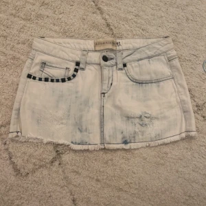 Vit jeanskjol med slitningar från Bershka - Säljer en vit jeanskjol från Bershka med coola slitningar och fransad nederkant. Kjolen har svarta rutdetaljer vid fickorna och klassisk femficksdesign. Perfekt för dig som gillar streetstyle och vill ha en edgy look. Så snygga detaljer med nitar och den perfekta ljusblå färgen! Köpt secondhand midjemått 37 💓 