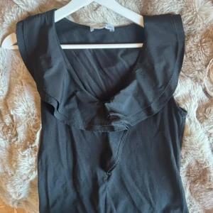 Svart klänning med volangkrage från MNG - Supersnygg svart klänning från Mango med bred volangkrage och ärmlös design. Klänningen har en v-ringning och är perfekt för dig som gillar stilrena och trendiga plagg. 