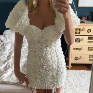 Vit studentklänning - Superfin vit kortklänning med 3D-blommor över hela tyget och puffiga ärmar. Klänningen har snörningsdetaljer framtill och markerad byst. Perfekt för studenten! Den är från Asos Luxe och säljs inte längre vad jag vet. Den är så fin, älskade den på studenten🥹❤️
