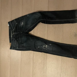 Dondup jeans  - Säljer ett par mörkblå dondup jeans med coola slitningar och detaljer på framsidan. Modellen har smal passform och klassiska fem fickor. Jeansen har kontrastsömmar och är tillverkade i jeansmaterial med stretch för extra komfort.