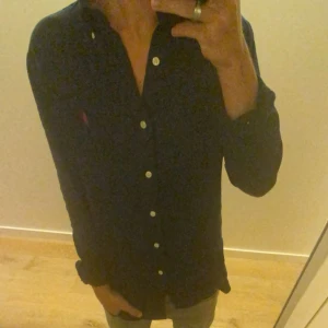 Mörkblå skjorta från Polo Ralph Lauren - Säljer för att den är lite föt stor stor!är 176. Storlek S, Snygg mörkblå skjorta från Polo Ralph Lauren med klassisk custom fit. Skjortan har långa ärmar, vita knappar och röd broderad logga på bröstet. Tillverkad i mjuk bomull och har en stilren krage. Perfekt för dig som gillar tidlös och clean stil.