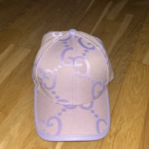 Ljuslila keps från Gucci - Säljer en snygg keps från Gucci i ljuslila och beige med GG-logga över hela kepsen. Kepsen har justerbart spänne bak i lila läder och är tillverkad i bomullsmix. Perfekt accessoar för att lyfta din outfit med exklusiv känsla.