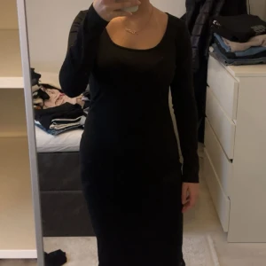 Svart långärmad klänning från Shein - En svart, figurnära långärmad klänning från Shein med rundad, djup urringning. Klänningen är enkel och stilren, går ned till knäna och har en tight passform som framhäver siluetten. Perfekt för dig som gillar minimalistisk och clean stil.