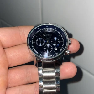 Silverfärgad Faucon herrklocka - Snygg herrklocka från Faucon med mörkblå urtavla och silverfärgat armband i metall. Klockan har tre små kronografer, datumvisning och stilrena indexmarkeringar. Perfekt accessoar för dig som gillar klassisk design med modern touch. Nypris är ca 2500 kr.