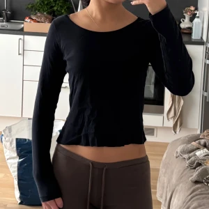 Svart croppad långärmad topp - Säljer en svart, croppad långärmad topp med rund hals. Toppen har en enkel och clean design med lätt vågad kant nedtill. Perfekt för dig som gillar basic plagg med snygg passform. Materialet känns mjukt och stretchigt, troligen bomull eller polyester.