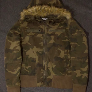 Camouflage bomberjacka från Jaded London - Säljer en fett snygg bomberjacka från Jaded London i camouflage-mönster. Jackan har huva med fejkpäls, ribbade muddar och flera fickor med dragkedja. Materialet är bomull och polyester, perfekt för höst och vinter. Passformen är normal och jackan är långärmad. Den är knappast använd och nypris är 2600 kr. Bild nr 4 är inte min bild men det är bara passform. Skriv om frågor och prisförslag! 🙏