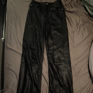 Svarta raka byxor i skinn från Zara - Snygga svarta byxor från Zara i storlek 34, tillverkade i skinnimitation. De har klassisk femficksdesign, raka ben och knappstängning fram. Perfekta för dig som vill ha en cool och stilren look med edge.