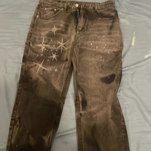 Unika svarta jeans med stjärnmönster - Säljer ett par svarta jeans med coolt stjärnmönster och blekta detaljer. Jeansen har klassisk femficksdesign och raka ben. Materialet är jeans och passformen är normal. Perfekt för dig som vill sticka ut med en unik look.