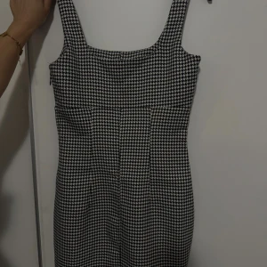Svartvit rutig klänning från Divided H&M - Supersnygg svartvit klänning från Divided i klassiskt hundtandsmönster. Modellen är ärmlös med breda axelband och har en figurnära passform. Perfekt för dig som gillar retrovibbar och vill sticka ut med ett coolt mönster. Har använt den bara 2 gånger.