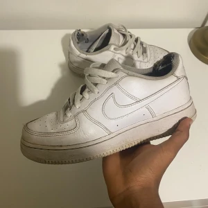 Nike Air Force 1 vita sneakers - Klassiska Nike Air Force 1 sneakers i helvitt skinn med rund tå och snörning. Snygg och tidlös modell med perforerade detaljer på tån och den ikoniska swoosh-loggan på sidorna. Perfekta för dig som gillar streetstyle och vill ha en clean look.