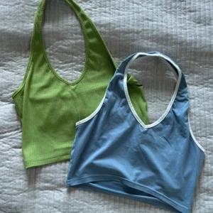 Grön och blå croppad linnetopp - Två croppade linnetoppar säljes! Ena är ljusgrön med ribbad struktur och v-ringning, den andra är ljusblå med vit kant och v-ringning. Båda är ärmlösa och har halterneck. Perfekt för sommarens alla dagar, superfräscha färger och skön passform.