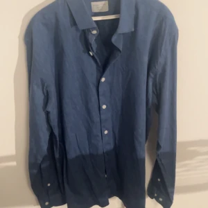 Blå linneskjorta från Selected Homme  - Snygg blå skjorta från Selected Homme i slim fit-modell. Tillverkad i svalt linne med klassisk krage och vita knappar framtill. Perfekt för dig som gillar stilren och enkel design med en modern passform.