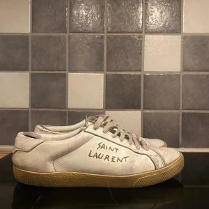 Saint Laurent vita skor - Säljer ett par vita Saint Laurent sneakers med handskriven logga på sidan. Använda väl därav priset. En lagning i hälkappan och på sidan, kan skicka bild vid förfrågan. Storlek 43 (passar 42, 44)