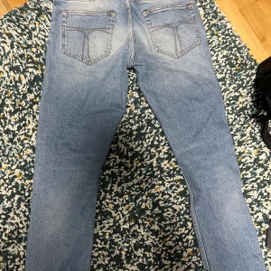 TIGER OF SWEDEN  - Säljer ett par tiger of sweden jeans i ljusblå tvätt med klassisk femficksdesign och snygga slitningar framtill. Jeansen har en slim passform och raka ben, perfekt för dig som gillar en modern och avslappnad stil. Materialet är mjukt jeans i bomull.
