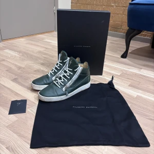 Giuseppe Zanotti gröna sneakers - Snygga gröna high-top sneakers från Giuseppe Zanotti i skinn med vita snören och silverfärgade dragkedjor på sidorna. Skorna har vit sula och klassisk rund tå. Kommer med originalkartong och dustbag. Perfekta för dig som vill sticka ut med stil. De är inte alls mycket använda och är helt äkta! De är i storlek 41 men passar 42.                    De har inte en ända defekt men är fick lite skitiga men for bara att tvätta bort!💪🏻 Hör av er för minsta lilla fundering!💯