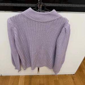 Ljuslila ribbad stickad polotröja - Säljer en ljuslila stickad polotröja med ribbad struktur. Tröjan har lång ärm och en bred, mjuk krage som ger en chill vibe. 