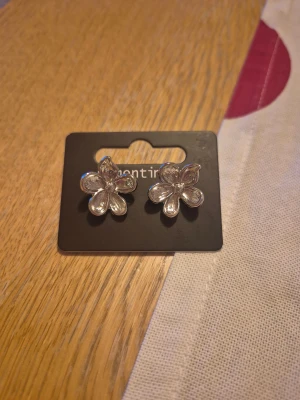 Silvriga blomformade örhängen -  ett par silvriga blomformade örhängen på ett svart kort. HELT NY OCH OANVÄND.