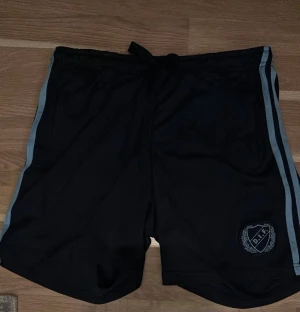 DIF shorts  - Svarta shorts med ljusgrå ränder längs sidorna och DIF-logga framtill. De har snörning i midjan för justerbar passform och är perfekta för sport eller chill. Materialet känns lätt och bekvämt, med en normal passform.