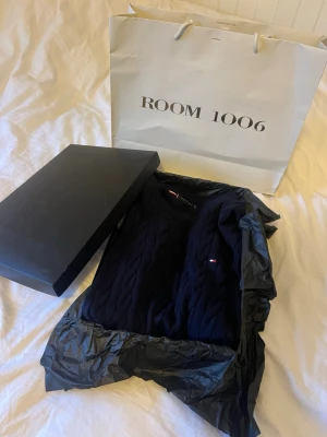 Mörkblå kabelstickad tröja Tommy Hilfiger - Snygg mörkblå kabelstickad tröja från Tommy Hilfiger i storlek L. Tröjan har rund hals, lång ärm och diskret logga broderad på bröstet. Perfekt för dig som gillar klassisk stil med en modern touch. Materialet är mjuk bomull som känns skönt mot huden.