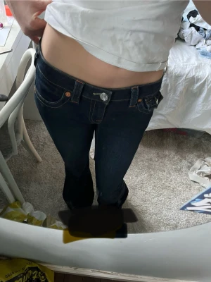 Mörkblå bootcut jeans låg midja - Snygga mörkblå jeans med låg midja och bootcut passform. Klassisk femficksmodell med kontrastsömmar och silverfärgad knapp. Perfekta för dig som gillar en retro vibe och vill ha ett par jeans som sitter tajt upptill och släpper vid benen.