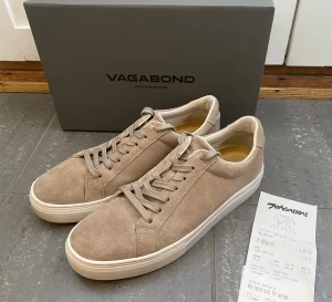 Beige Mockasneakers från Vagabond (Oanvända) - Snygga beige sneakers från Vagabond med ovandel i mjuk mocka och vita platta sulor. Skorna har rund tå, snörning och stilren design som passar till jeans eller shorts. Perfekta för dig som gillar minimalistisk och clean stil. Storlek 42 men passar mer som 43-44. Kvittot medföljer. Snabb Leverans!