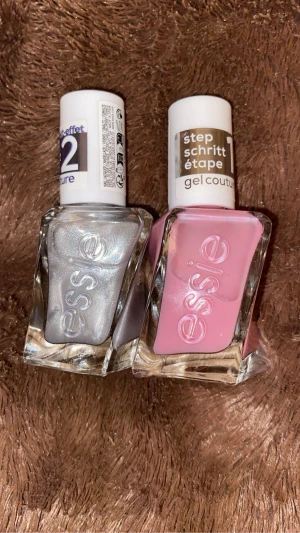 Essie gelcouture nagellack duo - Två Essie gelcouture nagellack i snygga flaskor med vriden design. Ena är metallic silver med skimrande finish, andra är ljusrosa med krämig look. Perfekt för att skapa trendiga naglar med salongskänsla hemma.
