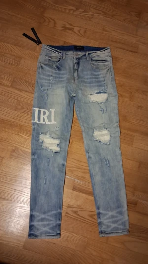Amiri jeans - Säljer ett par ljusblå jeans från Amiri med slitna detaljer och broderade bokstäver på benen. Det är storlek 36, de passar mig perfekt och jag är ca 186cm så skulle säga att de passar från 180-195 beroende på vad man väger. Jag har haft de i typ ett halvt år men har bytt stil de så därför säljer jag. Inga stora tecken på användning, perfekt skick. Pris: 1200 eller högsta bud