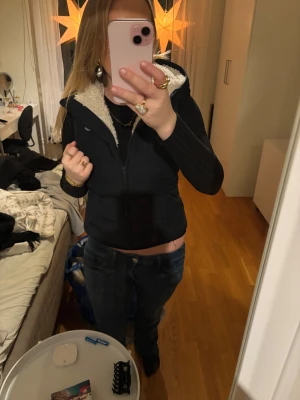 Svart pufferväst från Hollister - (Storleken är M men passar bra för xxs/xs/s) Svart pufferväst från Hollister med mysigt vitt teddyfoder på insidan och huva. Jackan har dragkedja framtill, broderad Hollister-logga på bröstet och en figurnära passform. Perfekt för kalla dagar när du vill vara både varm och snygg.