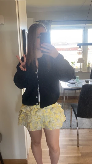 Gul volangkjol med blommigt mönster - Supersöt kort kjol i ljusgul med blommigt mönster och flera volanger. Kjolen har en flowy och lekfull form som ger extra rörelse. Perfekt för dig som gillar färg och detaljer! Materialet känns lätt och luftigt, idealiskt för varmare dagar.