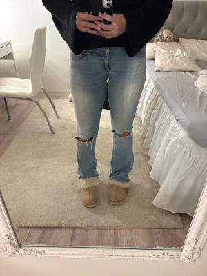 Ljusblå jeans med slitna knän - Säljer ett par ljusblå jeans med snygga slitningar vid knäna och klassisk fickdesign. Jeansen har en rak passform med något utsvängda ben och låg midja. Materialet är mjukt denim som ger en avslappnad vibe. Det är två knappar i midjan och jag är 170 och byxorna går hela vägen ner. Säljer dom då dom är för små😊