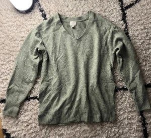 Grön v-ringad stickad tröja H&M - Snygg grön stickad tröja från H&M med v-ringad hals och ribbade muddar vid ärmslut och nederkant. Den har två slittar, på var sin sida nere vid midjan. Den är stor i storleken!
