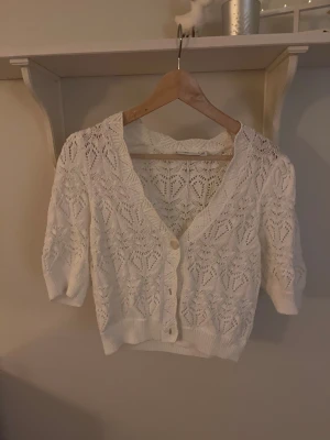 Vit stickad kofta med hjärtmönster - Superfin vit stickad kofta med korta ärmar och v-ringad hals. Koftan har ett detaljerat hjärtmönster och knappar framtill. Perfekt att slänga över en topp för en söt och chill look. Ribbad kant nedtill och vid ärmslut ger extra stilpoäng. Skriv för fler bilder/frågor❤️❤️