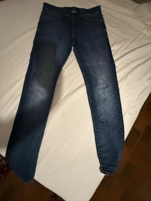 Blå jeans från Jack & Jones - Säljer ett par blå super stretch SLIM/GLENN jeans från Jack & Jones med klassisk femficksdesign och snygga slitningar. Jeansen har en rak passform och normal midja, med subtila detaljer på bakfickorna. Perfekt för dig som gillar stilrena och bekväma jeans. Priset går ner i snabb affär 