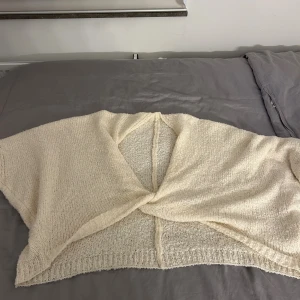 Stickad bolerotopp i ljusbeige - Mysig stickad bolerotopp i ljusbeige med twistad omlott-design framtill. Toppen är kort och har en lös passform med breda ärmar. Perfekt att slänga över en klänning eller linne för en chill look.