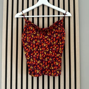 Blommig linnetopp från Zara XS - Superfin linnetopp från Zara i vinrött med blommigt mönster i orange och gult. Toppen har smala axelband, knappar framtill och en lätt croppad passform. Jättefin! Lite blankare silkes material. Knappliknande bak, se näst sista bild! 💕