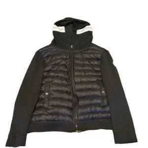 Svart dunjacka med huva från Moncler - Svart dunjacka från Moncler med quiltad front och släta ärmar. Jackan har huva med vit randdetalj, dragkedja framtill och två fickor med tryckknapp. Perfekt för kyliga dagar och snygg till streetwear.