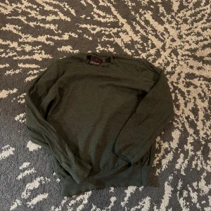 Mörkgrön stickad tröja från Oscar Jacobson - Mysig mörkgrön stickad tröja från oscar Jacobson med rund halsringning och långa ärmar. Perfekt för lager-på-lager och passar till både jeans och chinos. Enkel och stilren design som funkar året runt.