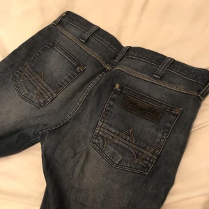  Wrangler jeans straight fit - Snygga mörkblå jeans från Wrangler med klassiska kontrastsömmar och broderade bakfickor. Modellen har raka ben och normal passform. Väldigt bra skick utöver en lite slitning längst ner på ena benet                                