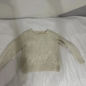 Beige kabelstickad tröja från Wera - Säljer en beige kabelstickad tröja från Wera med grovstickat mönster och rund hals. Tröjan har långa ärmar och bred ribbad mudd vid ärmslut och nederkant. Perfekt för lager-på-lager under kyliga dagar.